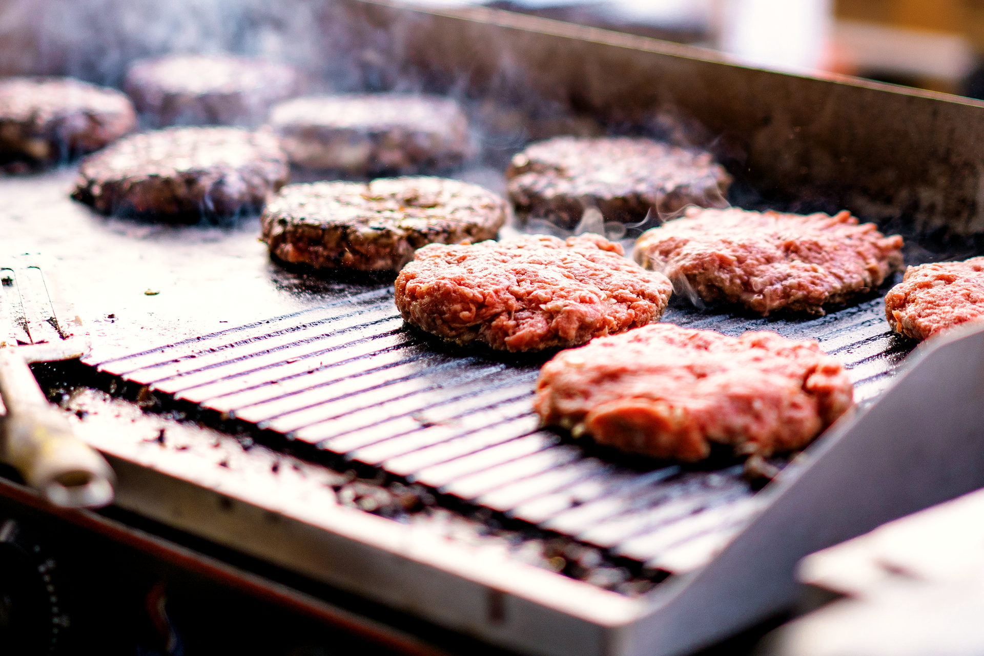 Varias carnes de smash en la plancha, con vapor saliendo de la parrilla.