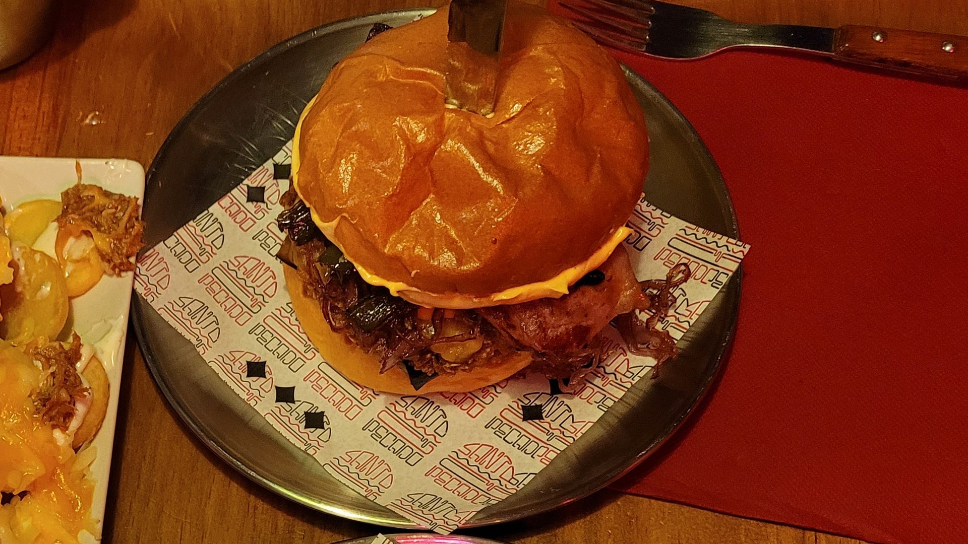 Primer plano de la burger con la loncha de queso todavía entera sobre la carne, sobre el papel de Santo Pecado.