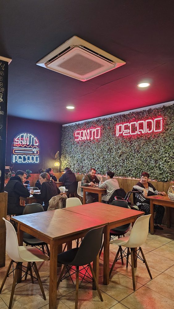 Salón del local de Daimús, con mesas de madera, el neón de Santo Pecado y la pared vegetal