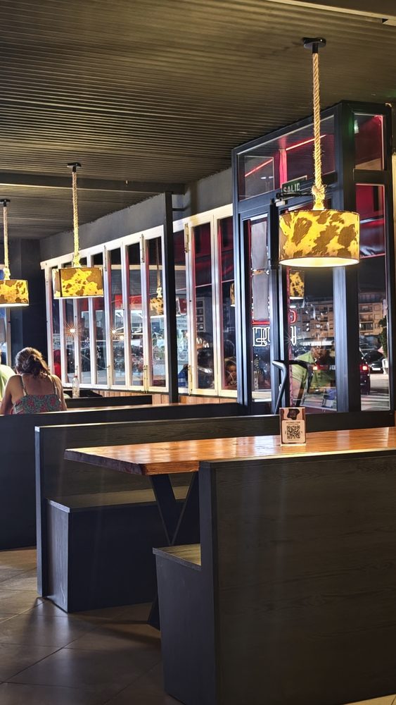 Salón del local de Playa de Gandia, con mesas de madera, lámparas colgadas y las ventanas a la calle
