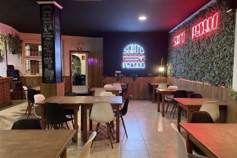 Sala de Santo Pecado Daimús: mesas de madera, la pared vegetal y los neones del local.